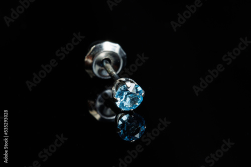 Silver earring macro photo with a precious stone on a black isolated background
