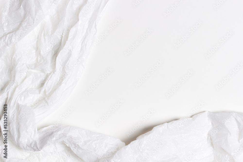 Obraz premium White plastic wrap background. Crumpled wrinkled plastic cellophane on blank white background. Reflecting light and shadow on creases and folds in plastic surface. Texture overlay effect template