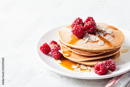 Stack of pancakes with raspberry, almonds and maple syrup on white plate. Breakfast food.