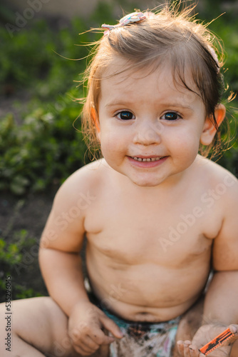 The portrait of a naked little girl, wearing only a diaper, sitting in her grandparents' garden in the village and playing with the soil. Letting touch the dirt