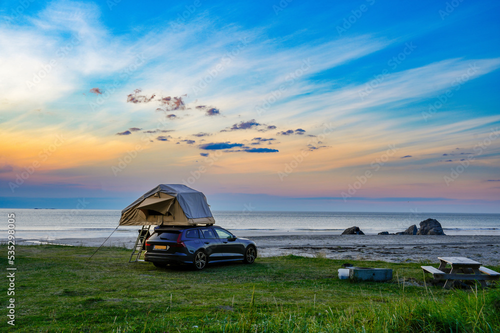 Camper mit Zelt auf dem Autodach am Strand bei Sonnenuntergang auf den Logoten - obrazy, fototapety, plakaty 