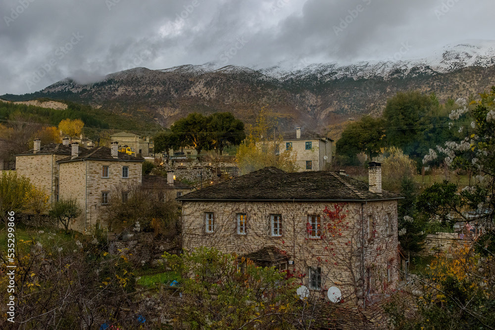 Τraditional architecture  with the stone buildings and snowy mountains as background during  fall season in the picturesque village of papigo , zagori Greece