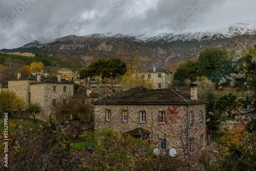 Τraditional architecture  with the stone buildings and snowy mountains as background during  fall season in the picturesque village of papigo , zagori Greece photo