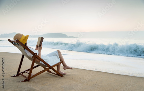 Bild auf Leinwand Young lady reading a book on the beach.