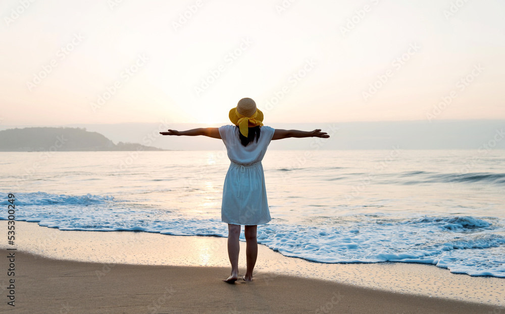 Happy woman standing on the beach with arms outstretched.