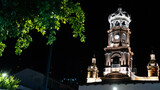 vista nocturna de torre de iglesia con corona en lo alto y arbol en primer plano, iglesia de Guadalupe en Puerto Vallarta México