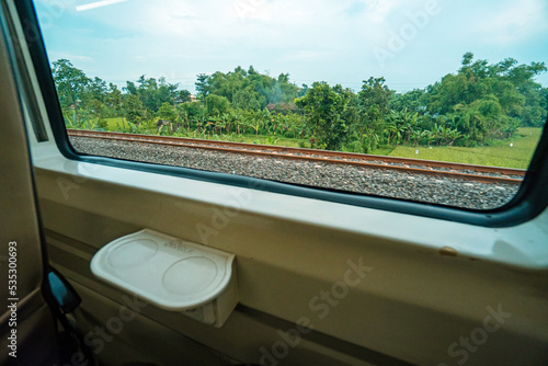 Riding a train in Indonesia sitting by the window watching the tracks and the view outside the window of the train speeding towards its destination