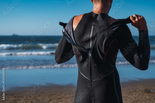 Man on the beach takes off his wet wetsuit after his surf lesson