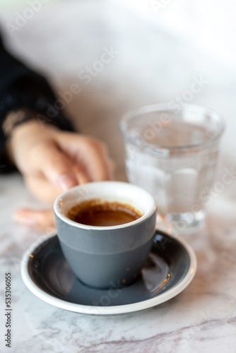Female hand holding cup of espresso. Morning ritual at the cafe.