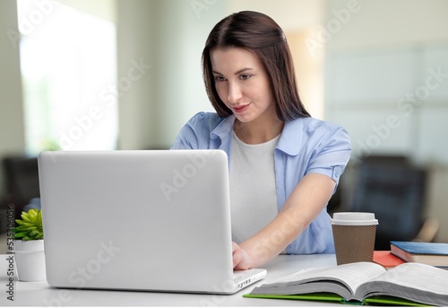 Cheerful business lady working on laptop in office. Attractive female employee office worker smile.