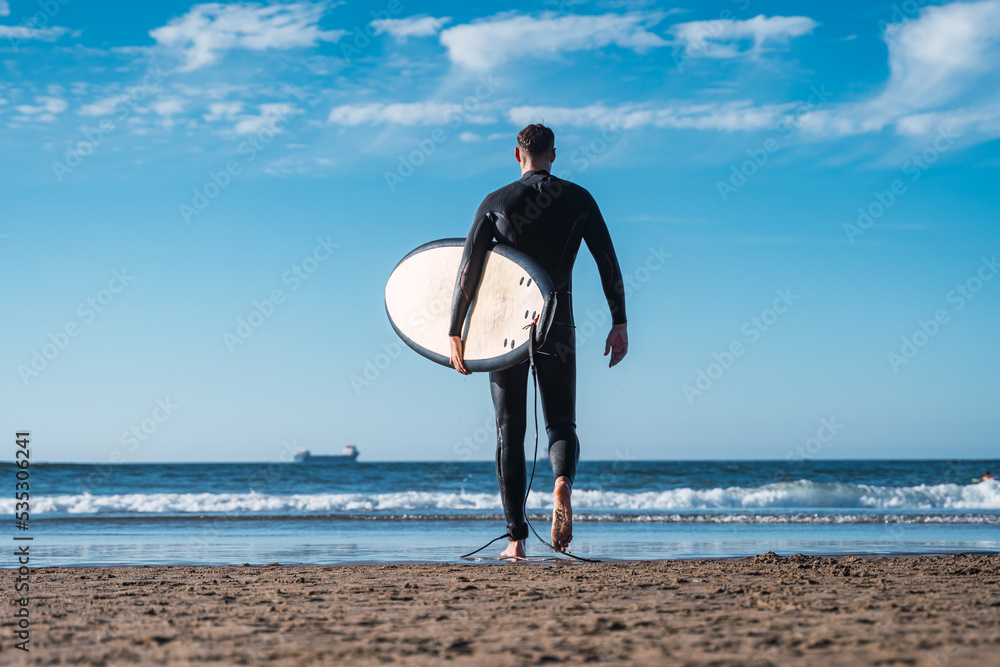 Young man walks along the sand of the beach to enter the sea and do his favorite sport. The surf