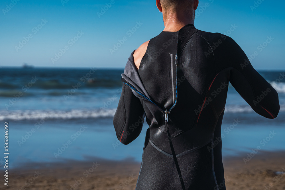 Man finishing surfing and removing the wet neoprene from his body.