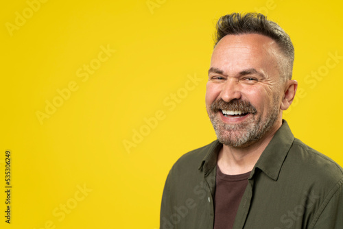Happy attractive handsome mature man with beard smiling isolated over yellow background. Active Positive middle-age person lifestyle concept. photo