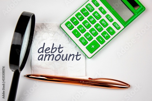 The words debt amount on crumpled paper next to a calculator and a magnifying glass. The concept of accumulated debt, write-off, study, recalculation.