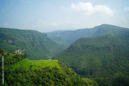 ravine trees and vegetation, view of several mountains at different depths, blue sky and few clouds, mexico