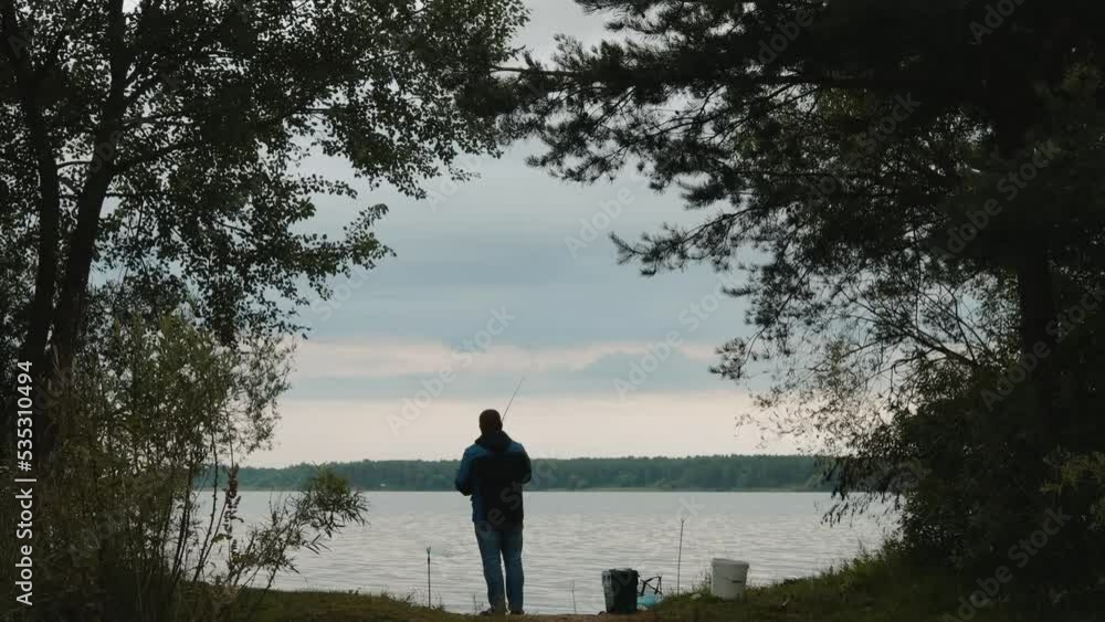 a fisherman reels off a fishing rod on the shore of the lake against the background of the morning sky a fisherman reels off a fishing rod on the shore of the lake against the background of the morning sky