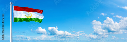 Tajikistan flag waving on a blue sky in beautiful clouds - Horizontal banner