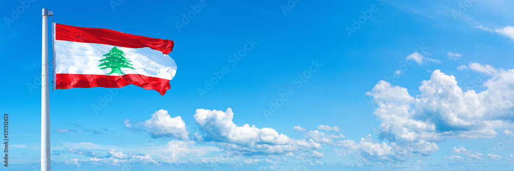Obraz premium Lebanon flag waving on a blue sky in beautiful clouds - Horizontal banner