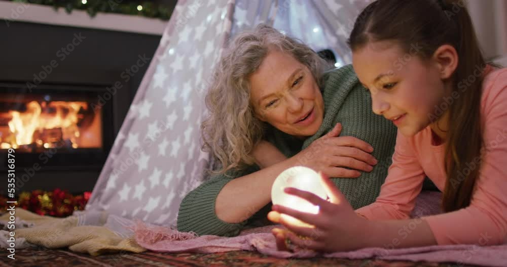Happy caucasian girl with grandmother playing with snow globe at christmas