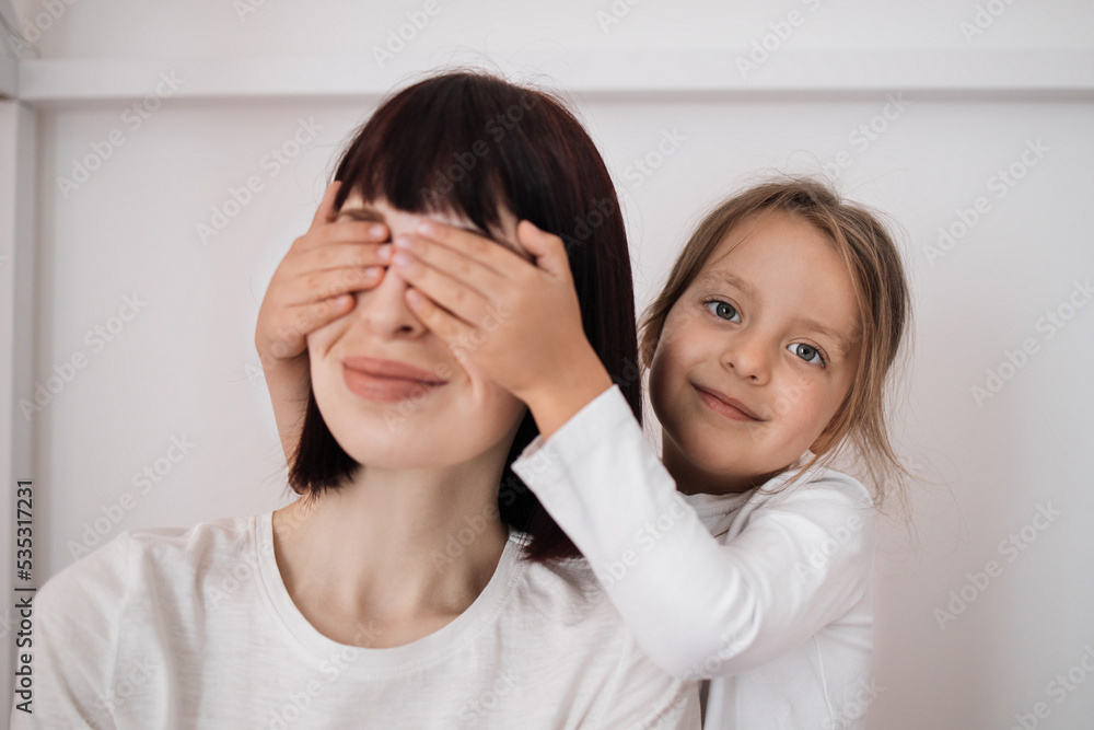 Satisfied caucasian preschooler girl closes eyes to young lady and congratulates with birthday, sitting on bed in bedroom interior. Surprise, holiday, love and relationship. Celebrate at home Satisfied caucasian preschooler girl closes eyes to young lady and congratulates with birthday, sitting on bed in bedroom interior. Surprise, holiday, love and relationship. Celebrate at home