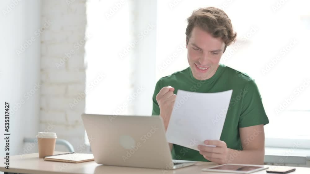 Young Man Cheering while Reading Business Report at Work Young Man Cheering while Reading Business Report at Work