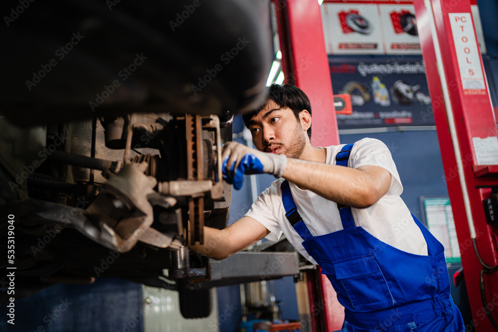 Asian auto mechanic in car garage. Vehicle service personnel are inspecting cars in mechanic factory with confidence in car engine repairs. Asian mechanic with equipment to fix cars in the service.