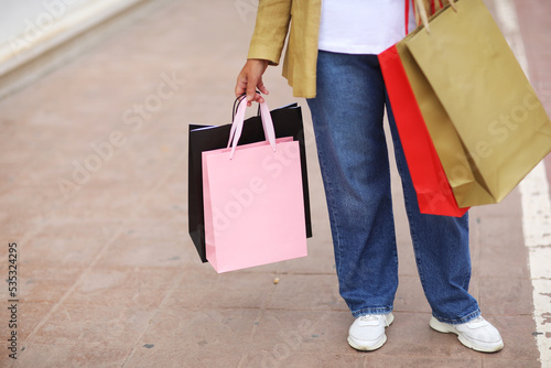 Cropped portrait of unrecognisable woman with colourful shopping bags on urban shopping mall background. Purchases, black friday, discounts, sale concept. Online shopping concept, Seasonal Sales.