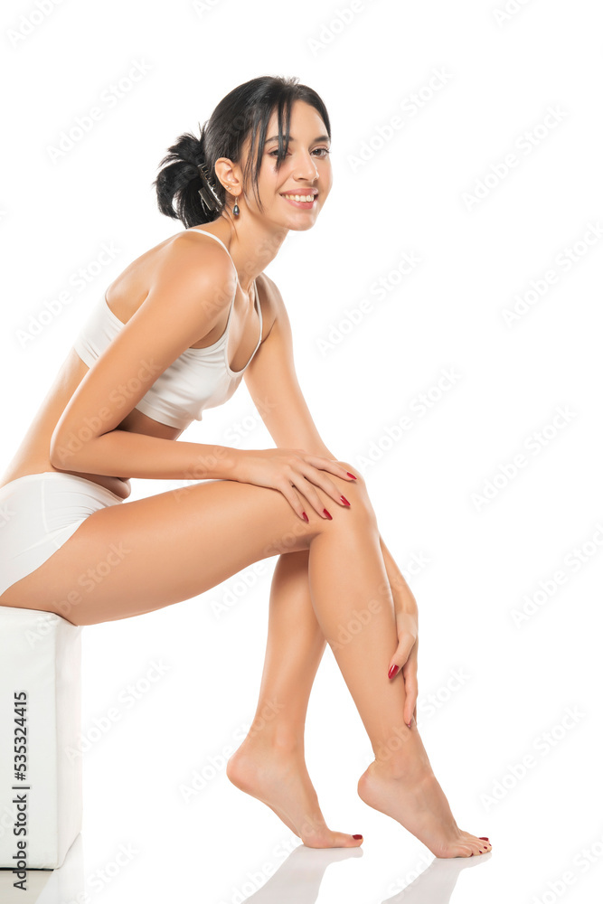 smiling young woman apply lotion on her legs on a white background.