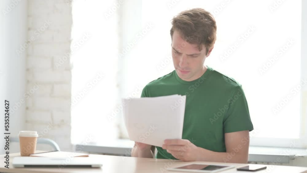 Young Man Upset while Reading Documents in Office Young Man Upset while Reading Documents in Office