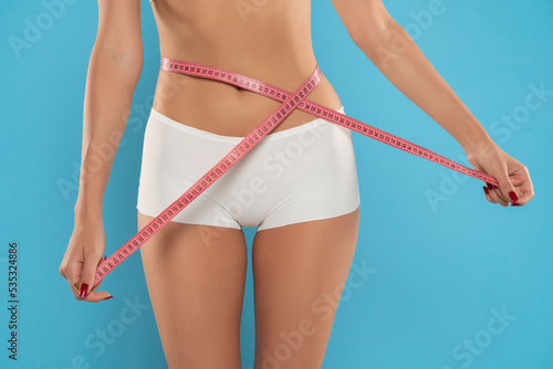 Woman measuring her waistline on a blue background. Perfect Slim Body