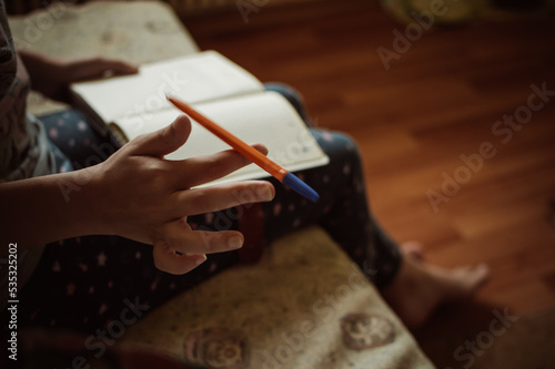 Girl with notebook twirls pen with her fingers sitting at home