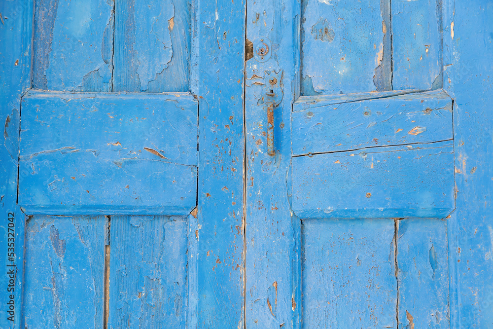 Wooden blue closed peeled door with rusty metal handle background. Greek island construction. Wooden blue closed peeled door with rusty metal handle background. Greek island construction.