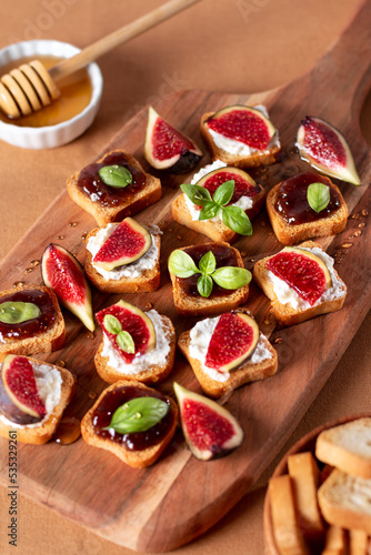 Toasts with figs, ricotta and fig marmalade sprinkled with honey on wooden board