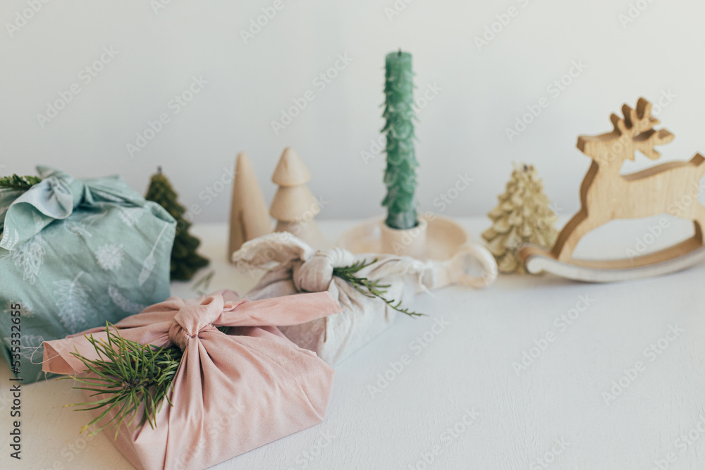 Stylish wrapped gifts in linen fabric on white rustic table with eco friendly wooden toys, fir branches, candle. Furoshiki gift wrapping. Zero waste Christmas. Happy Holidays! Space for text Stylish wrapped gifts in linen fabric on white rustic table with eco friendly wooden toys, fir branches, candle. Furoshiki gift wrapping. Zero waste Christmas. Happy Holidays! Space for text