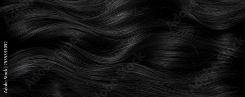 Brunette or black hair. Female long dark hair in black. Beautifully laid curls. Closeup texture in a dark key. Hairdressing, hair care and coloring. Shading gray hair. Background with copy space.