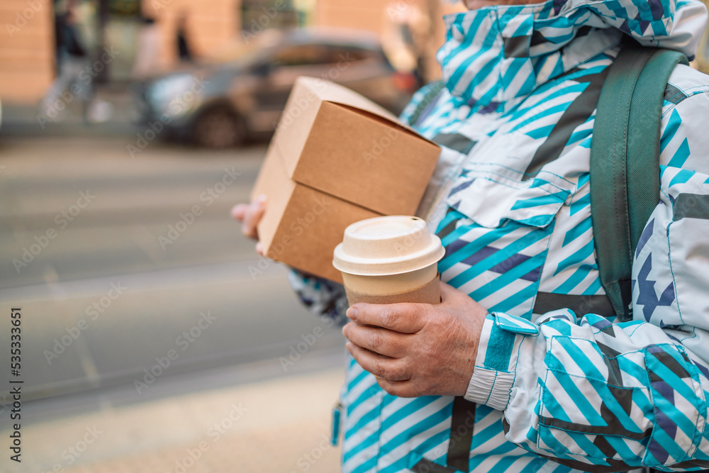 Stack of food delivery boxes. Anonymous hands holding stack of delivery boxes and coffee cup outdoors.Craft packaging of delivered food in hands. Stack of food delivery boxes. Anonymous hands holding stack of delivery boxes and coffee cup outdoors.Craft packaging of delivered food in hands.