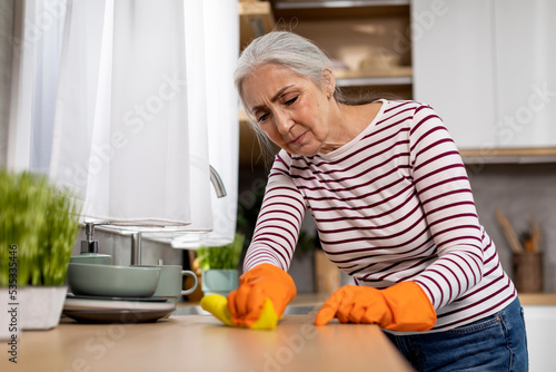 Household Duties. Tired Senior Woman Cleaning Table In Kitchen With Rag
