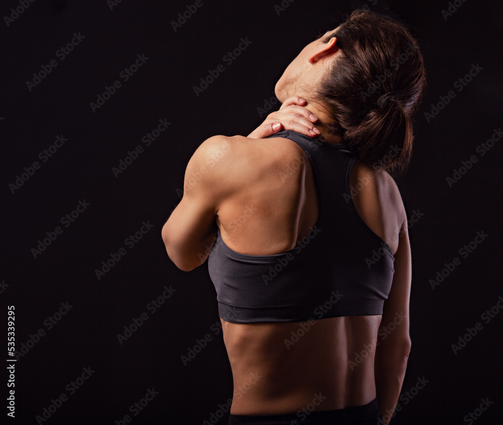 Sporty woman doing hand the massage to relax the tension in shoulder and neck in sport bra top on empty copy space black studio background. Closeup back view. Sporty woman doing hand the massage to relax the tension in shoulder and neck in sport bra top on empty copy space black studio background. Closeup back view.