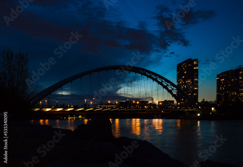 Evening city - arch suspension bridge, night lights, people walking and beautiful evening sky