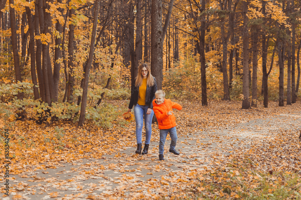 Mother and son walking in the fall park and enjoying the beautiful autumn nature. Season, single parent and children concept.