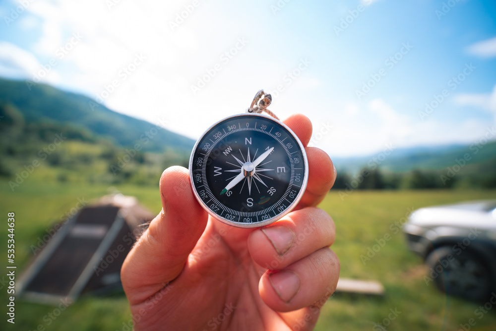 Travel magnetic compass male hand on background of mountain ridge in summer outdoor, point of view. Close up