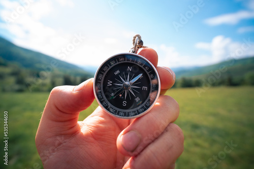 Travel magnetic compass male hand on background of mountain ridge in summer outdoor, point of view. Close up
