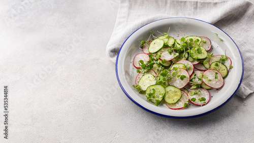Fresh salad of radish, cucumber and microgreens in a flat plate on a light background with copy space