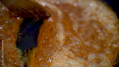 Slow motion of a wooden stick mixing heated and melted caramel sugar syrup in a hot pan, sweet sugary dessert preparation process