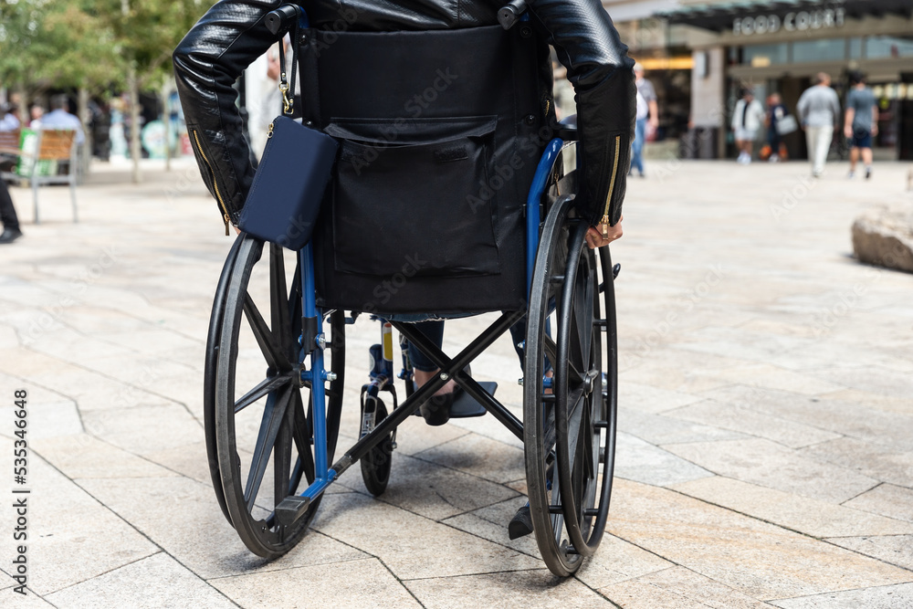 Obraz premium Young woman living life with disability wheeling herself around in a wheelchair in an outdoor shopping center