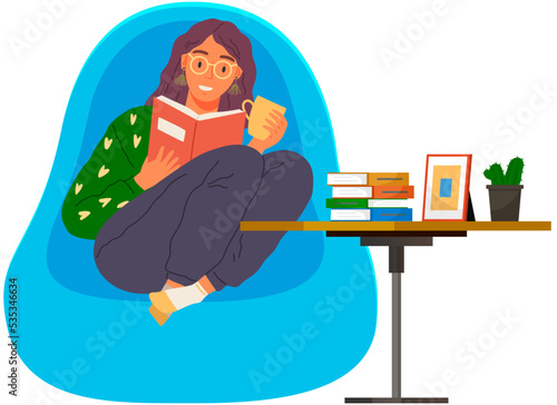 Young woman reading book, sitting on pillows in modern chair. Leisure and education. Relaxation with literature. Girl relaxing at home and drinking coffee. Student reads textbook holds cup in hand