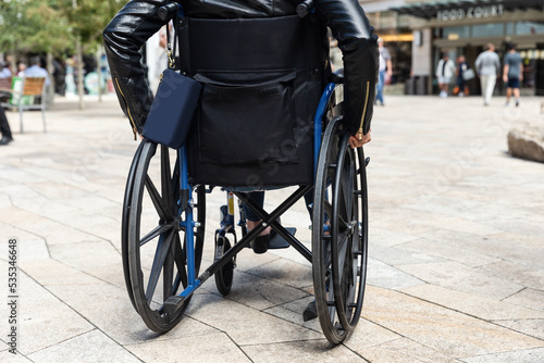 Young woman living life with disability wheeling herself around in a wheelchair in an outdoor shopping center © TS