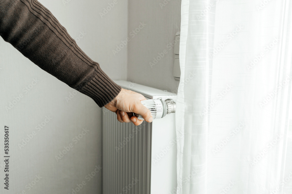 A man regulates the temperature on the radiator at home. Rising prices for heating in households. The concept of the energy crisis in Europe A man regulates the temperature on the radiator at home. Rising prices for heating in households. The concept of the energy crisis in Europe