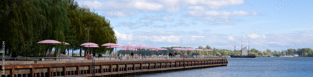 Web banner of a sailboat sailing with the pink beach umbrellas and Muskoka chairs in the foreground