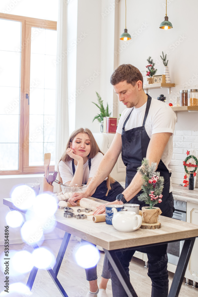 Young happy couple enjoying and preparing christmas cookies together in their kitchen. Young happy couple enjoying and preparing christmas cookies together in their kitchen.